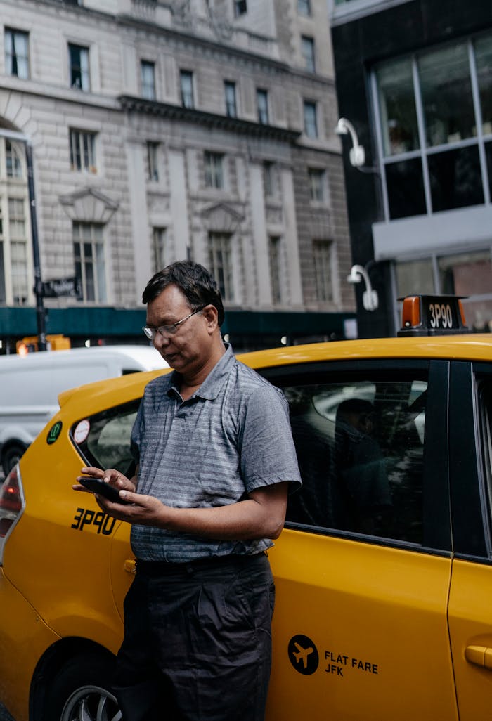 Ethnic man standing near taxi with smartphone